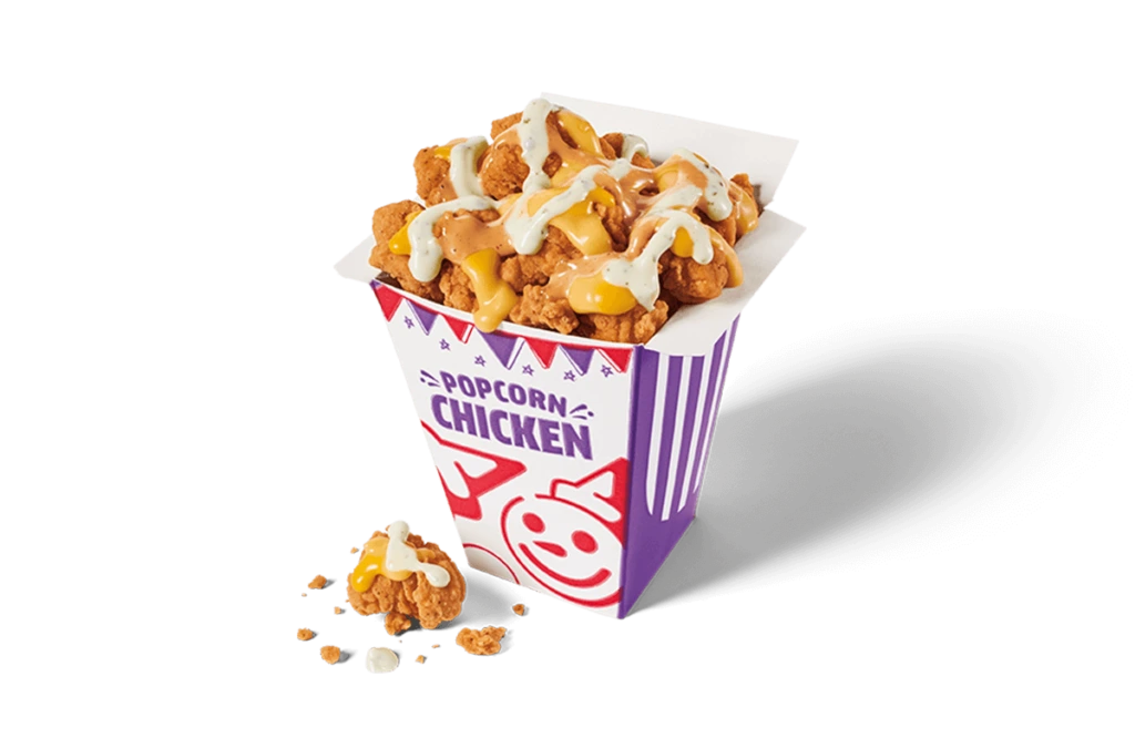 A fun and colorful carton brimming with popcorn chicken drizzled with creamy white and tangy yellow sauces. The crispy chicken pieces are nestled tightly together, showcased in a white and purple striped carton with playful designs, scattered with crumbs on transparent background.