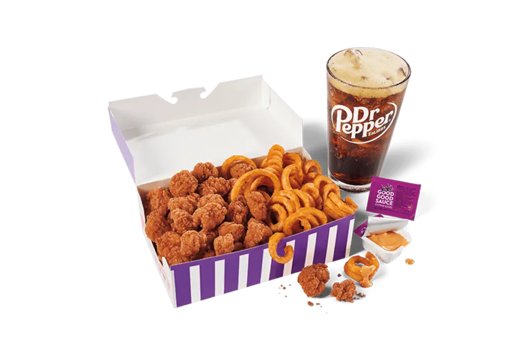 A large serving of spicy popcorn chicken and curly fries in a striped purple and white box, accompanied by a glass of Dr Pepper with a foamy head, and a sachet of sauce, presented on transparent background.
