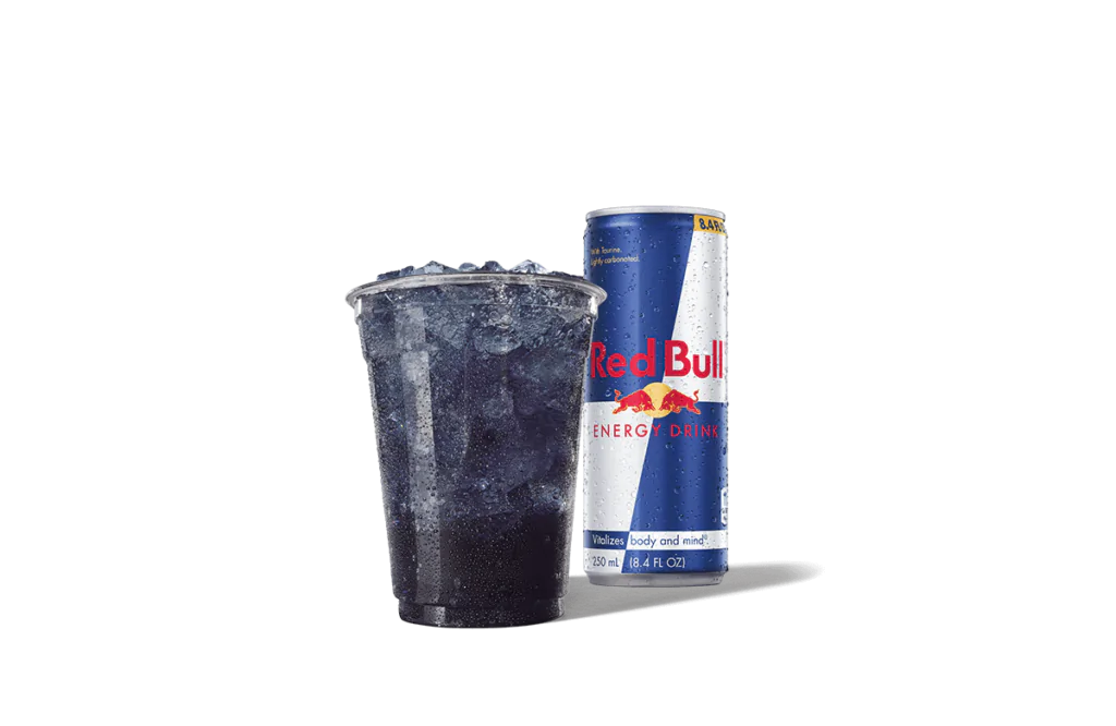A refreshing Berry Purple Daze Red Bull® Infusion drink from Jack in the Box. The image showcases a chilled, purple-infused drink in a transparent cup filled with ice, accompanied by a can of Red Bull® Energy Drink in its signature blue and silver design. Water droplets cover the can, emphasizing its icy, refreshing appeal.