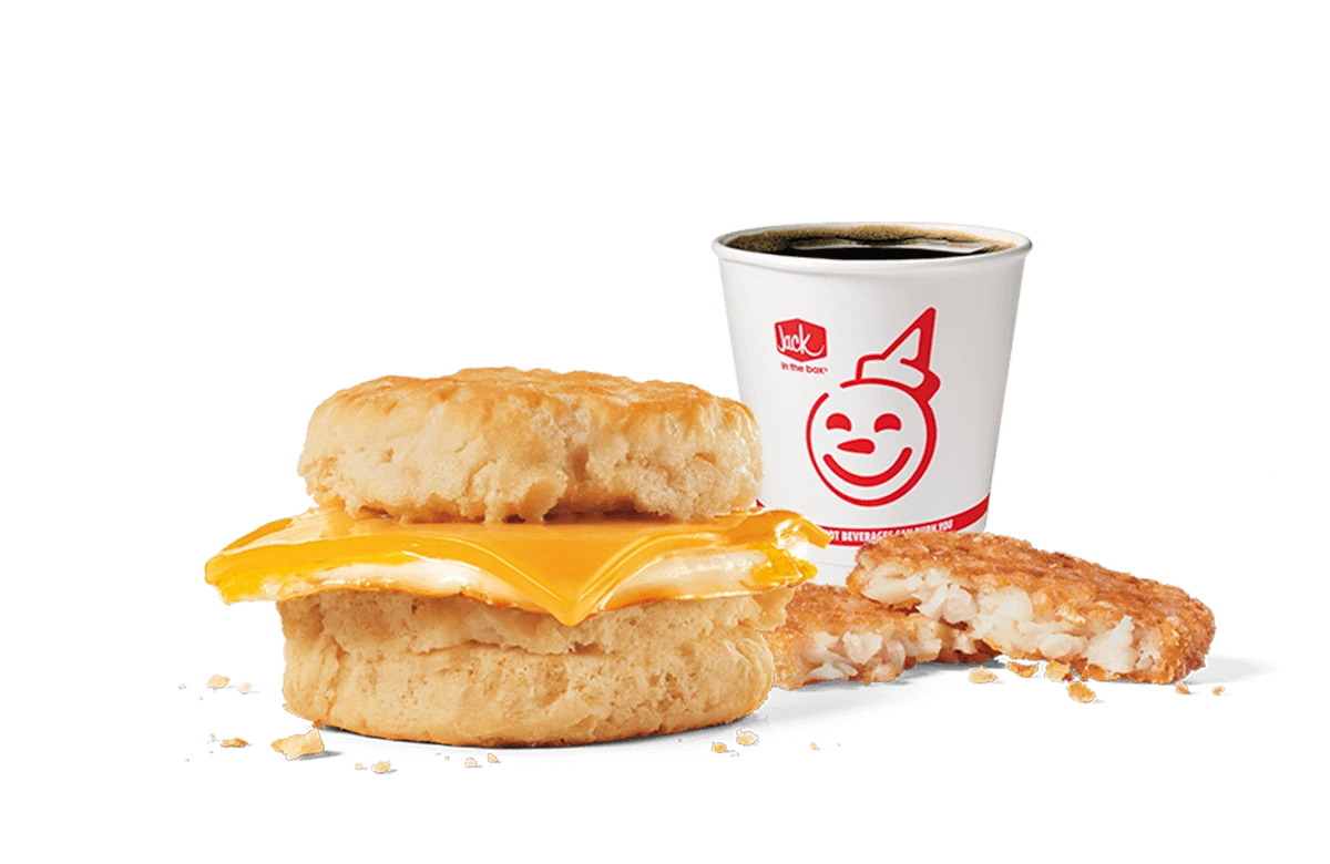 A simple yet satisfying breakfast combo from Jack in the Box featuring a biscuit sandwich with a fried egg and melted cheese, accompanied by a hash brown patty and a cup of hot coffee, presented on a transparent background with the restaurant's iconic smiling logo on the cup.
