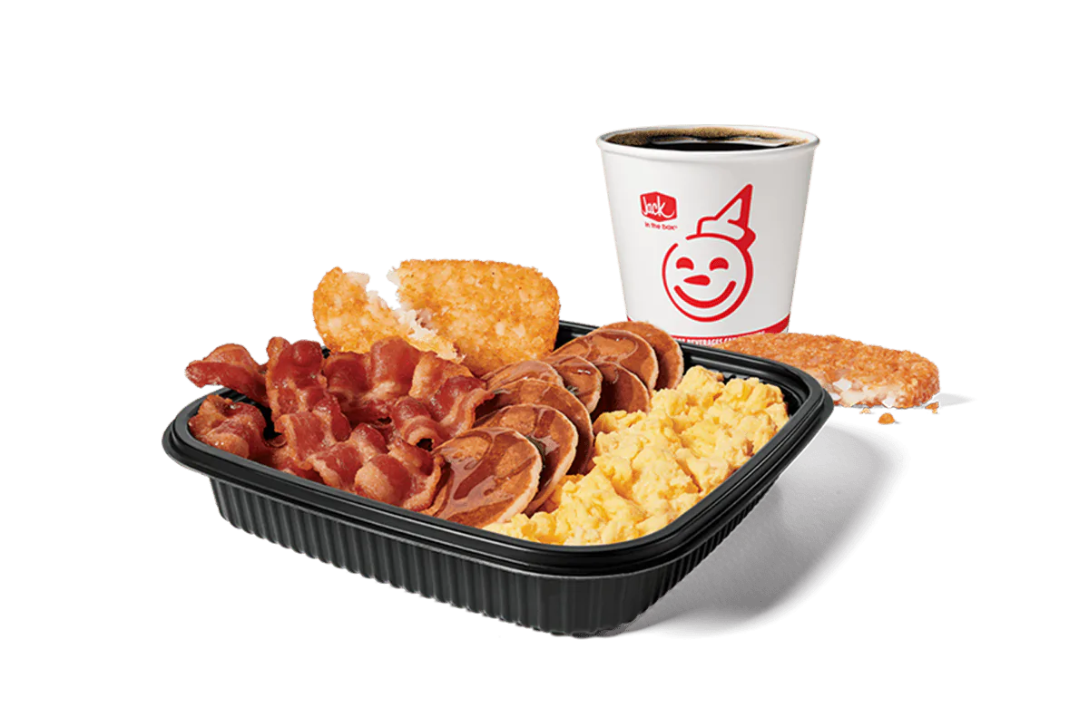 A mouth-watering Jumbo Breakfast Platter from Jack in the Box, featuring scrambled eggs, crispy bacon, hash browns, and mini pancakes, paired with a hot coffee. The meal is set against a transparent background, ideal for a filling and delicious breakfast.