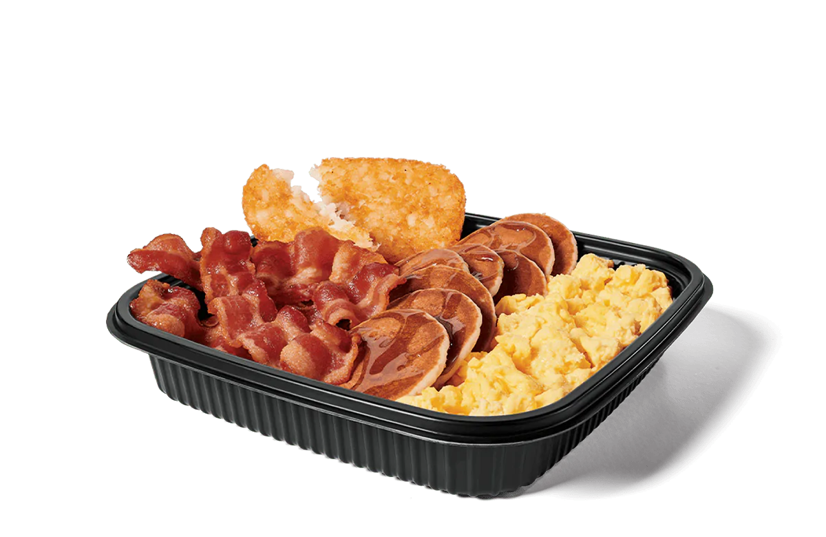 Image of a jumbo breakfast platter filled with crispy bacon strips, fluffy scrambled eggs, golden hash browns, and mini pancakes topped with syrup, served in a convenient black takeout tray.