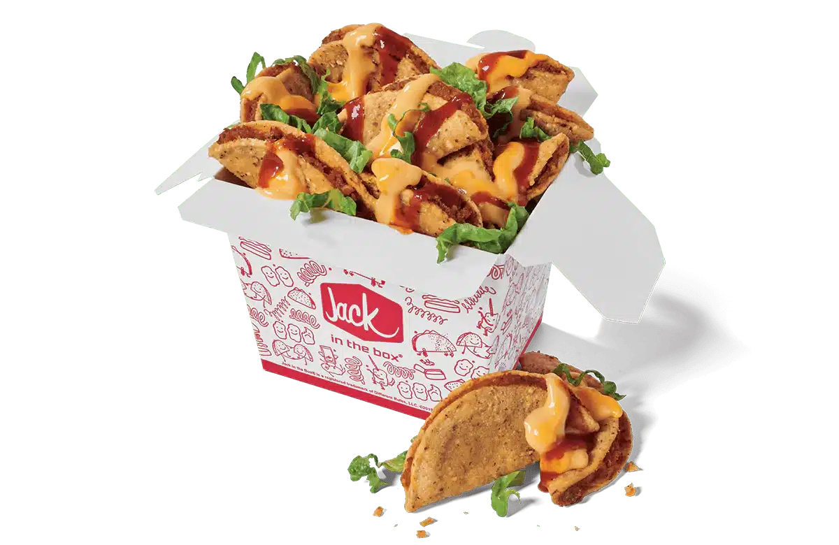 A box of Loaded Tiny Tacos from Jack in the Box. The tacos are served in a white box decorated with red illustrations and the Jack in the Box logo. Each taco is filled with seasoned meat, topped with melted cheese, a drizzle of taco sauce, and fresh shredded lettuce. A few tacos are spilling out of the box for an appetizing display against a transparent background.