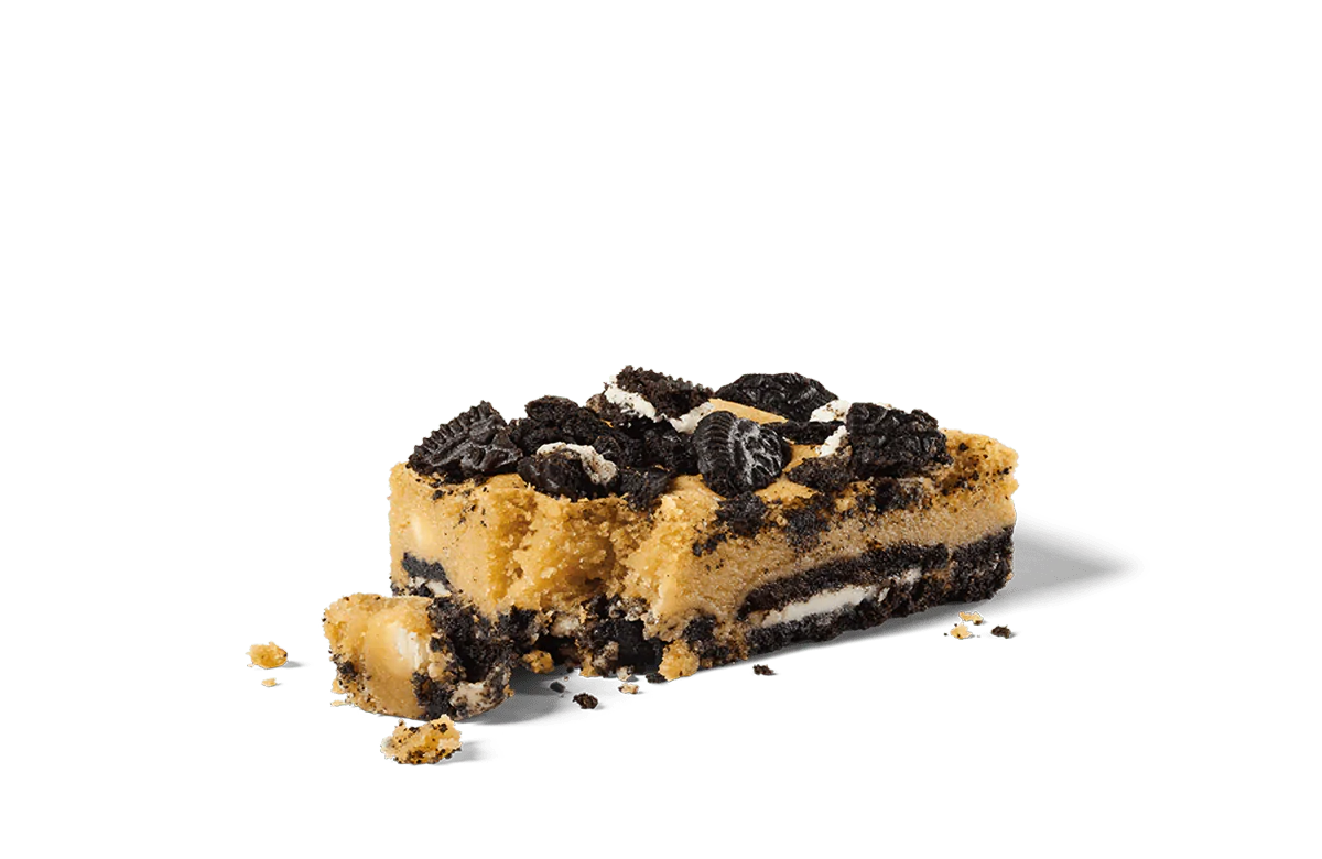 A decadent slice of Oreo® Ultimate Cookie Bar on transparent background, featuring layers of creamy filling and Oreo® cookie pieces. The top is generously sprinkled with crumbled Oreo® cookies, adding a rich texture and deep chocolate flavor to the dessert. The bar is showcased with crumbs scattered around, highlighting its freshly cut and indulgent appearance.