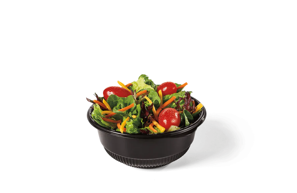 A fresh side salad in a small black bowl, featuring mixed greens, cherry tomatoes, shredded carrots, and shredded cheese.