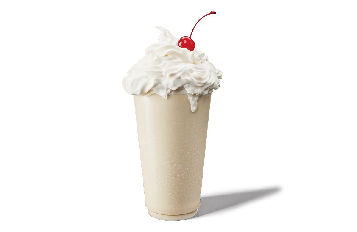 A classic vanilla milkshake in a tall glass, overflowing with whipped cream and topped with a single bright red cherry. The glass shows a refreshing condensation and the background is transparent, enhancing the simplicity and appeal of the milkshake.