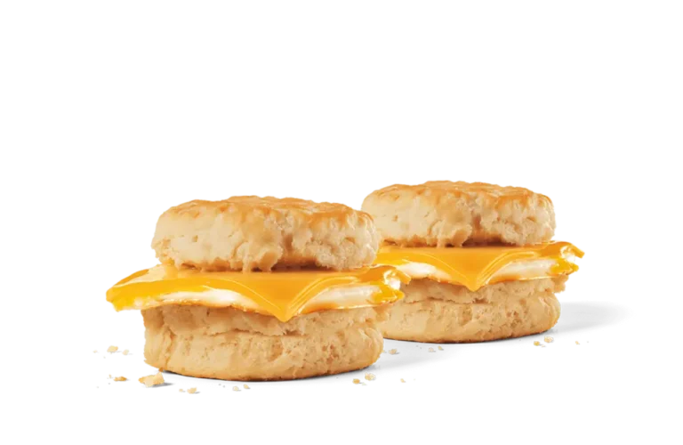 Two fluffy breakfast biscuits topped with a slice of melted cheese, presented on a transparent background.