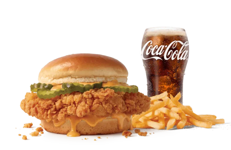 The Cluck Sandwich Combo features a crispy chicken fillet topped with melty cheese and pickles on a soft bun, served alongside golden fries and a chilled glass of Coca-Cola, presented against transparent background.