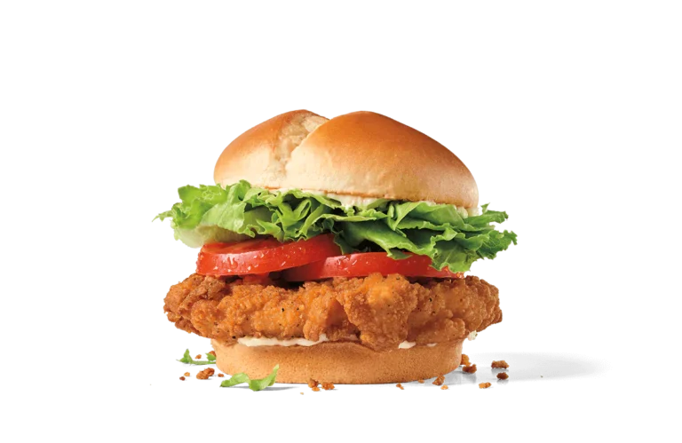 A stacked spicy chicken sandwich with a crispy breaded chicken patty, layers of fresh green lettuce, juicy tomato slices, and topped with a golden toasted bun, presented on a transparent background with crumbs scattered around.