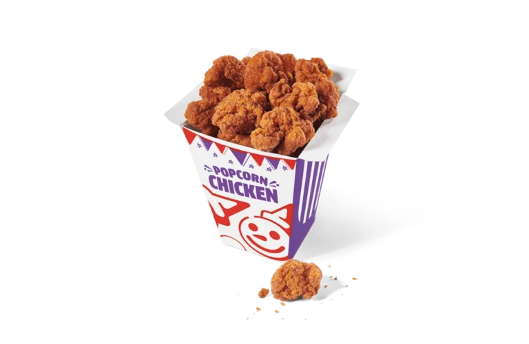 A carton filled with spicy popcorn chicken pieces, presented on transparent background. The chicken is deep-fried to a crispy golden brown, and the colorful carton is adorned with playful graphics and purple stripes, with some crumbs scattered beside it.