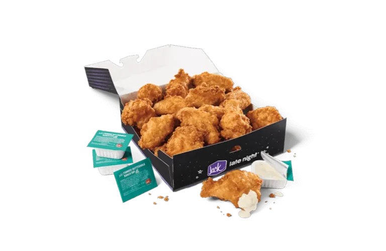 An 18-piece Classic Crispy Chicken Wings box from Jack in the Box, featuring golden, perfectly fried chicken wings. The wings are served in a sleek black box with the "Jack late night" branding. Surrounding the box are dipping sauces and condiment packets, including creamy ranch dressing, completing the meal's presentation.