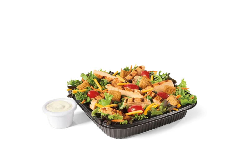 A fresh garden salad featuring mixed greens, cherry tomatoes, shredded cheese, grilled chicken strips, croutons, and a side of creamy ranch dressing in a small container.