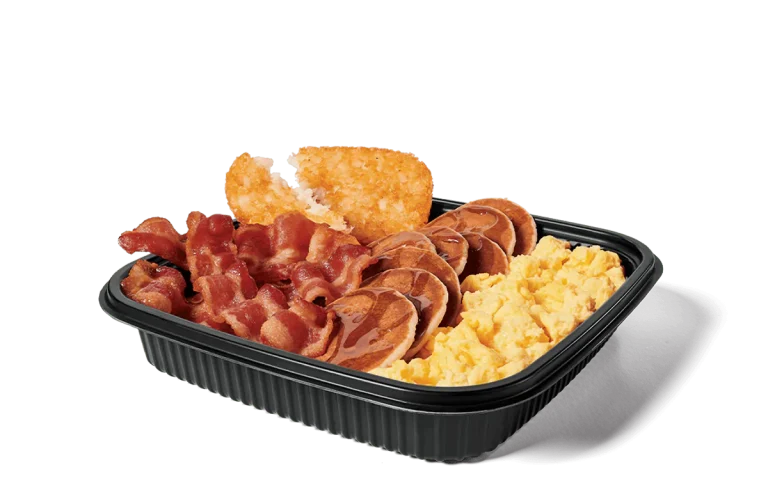Image of a jumbo breakfast platter filled with crispy bacon strips, fluffy scrambled eggs, golden hash browns, and mini pancakes topped with syrup, served in a convenient black takeout tray.