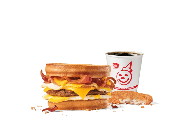 Image of the Loaded Breakfast Sandwich Combo from Jack in the Box, featuring a hearty sandwich with crispy bacon, a sausage patty, egg, and cheese between toasted sourdough bread. Served with a hash brown and a cup of coffee, all presented against a transparent background with the cheerful Jack in the Box logo.