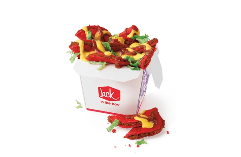 A box of sauced and loaded spicy tiny tacos from Jack in the Box, featuring red spicy mini tacos topped with melted cheese, tangy sauce, and fresh lettuce. The tacos are served in a branded white box with a red "Jack in the Box" logo, with some tacos placed outside the box for display.