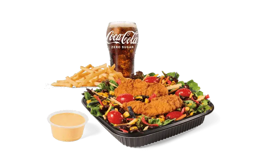 A Southwest-style salad featuring mixed greens, crispy chicken strips, cherry tomatoes, shredded cheese, colorful tortilla strips, and a side of spicy dressing. Served with a side of French fries and a Coca-Cola Zero Sugar drink.