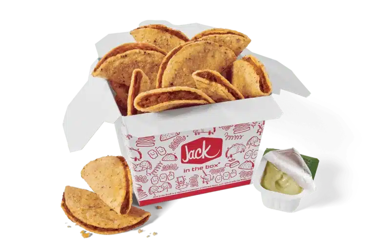A box of Tiny Tacos from Jack in the Box. The tacos are packed in a white box decorated with red illustrations and the Jack in the Box logo. The tacos have crispy shells and are filled with seasoned meat. Some tacos are displayed outside the box for emphasis. A small dipping cup with partially opened lid, filled with green avocado lime sauce, is included on the side. The image has a transparent background.