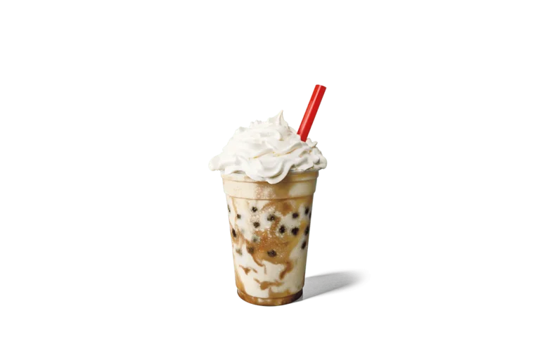 A refreshing vanilla shake speckled with dark boba pearls, served in a clear cup and topped with a lavish swirl of whipped cream. A red straw accents the creamy texture, set against transparent background that enhances the drink's visual appeal.